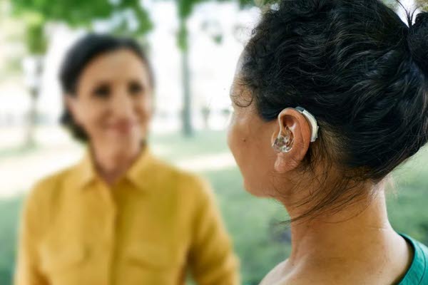 Två personer står mittemot varandra. Den ena bär hörapparat. Foto