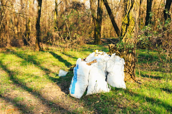 Fyra sopsäckar står i en skog. Foto.