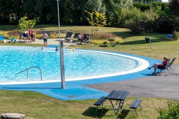 En utomhusbassäng med en utomhusdusch i förgrunden. Foto.