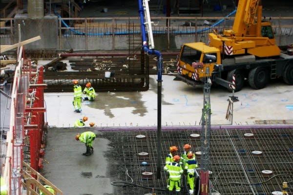 En industriarbetsplats med ett flertal människor som bär arbetskläder och skyddshjälm. Foto.