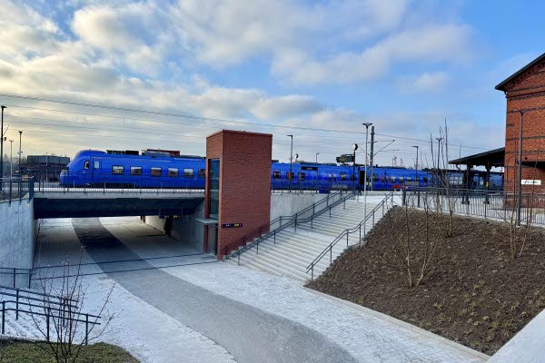 Folksamling framför stationshuset som är i rött tegel. Foto.