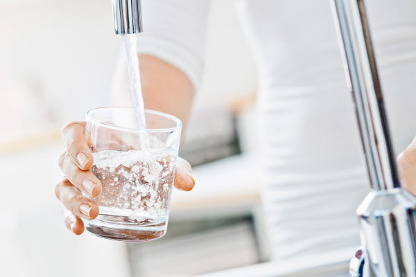 Hand håller ett glas under en rinnande kran med vatten, foto.