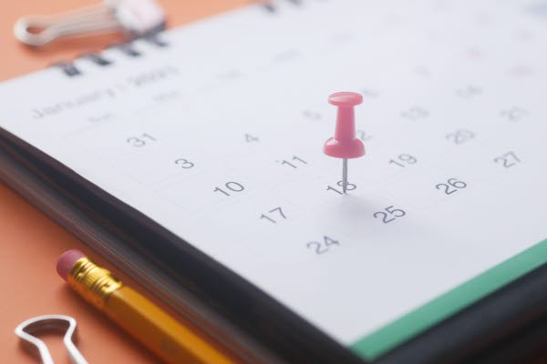 Ett rött häftstift placerat i en kalender på dag 18, foto.