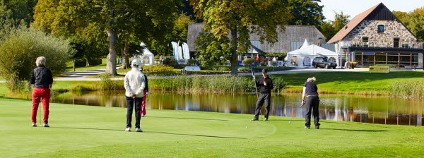 Golfspelare på banan med klubbhus i bakgrunden. Foto.