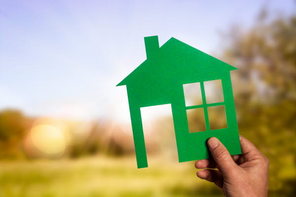 En hand håller en grön siluett av ett hus i papper, foto.