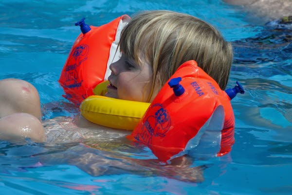 Ett barn som bär simredskap i en bassäng. Foto.