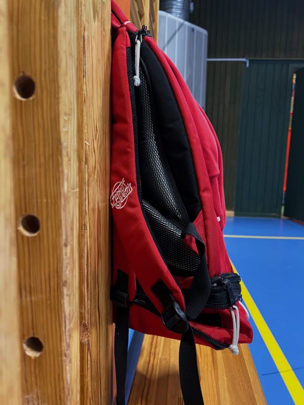 Röd och svart ryggsäck hängandes på en ribbstol i kyrkskolans jympasal