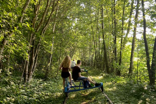 Två personer åker dressin genom en skog. Foto.