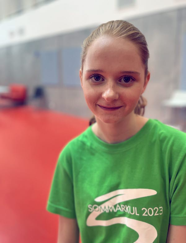 Flicka med rött uppsatt hår, bär en grön t-shirt med texten " Sommarkul 2023". Foto.