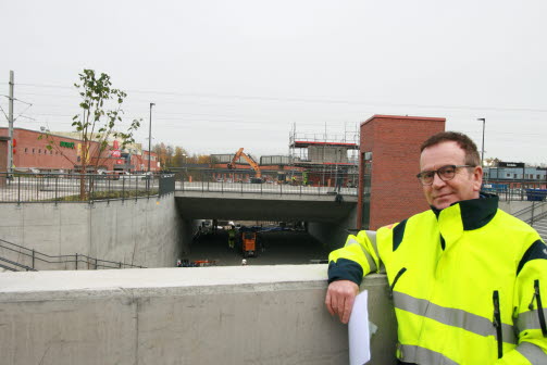 En person i gul reflexväst hänger med armen på en mur framför en tunnel. Foto.