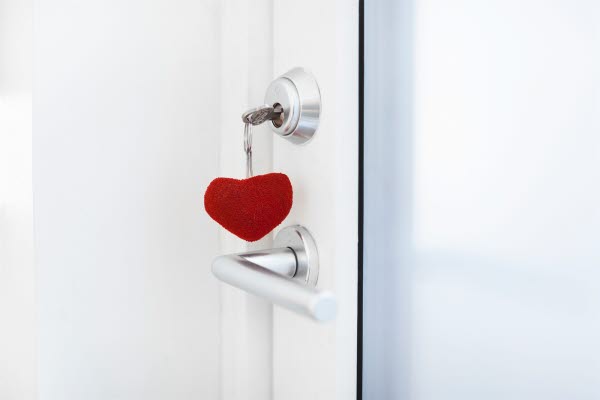 Nyckelknippa med ett rött hjärta och en nyckel som sitter i ett dörrlås på en vit dörr, foto.