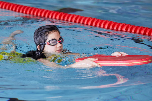 Ett barn simmar i en bassäng med hjälp av simredskap. Foto.