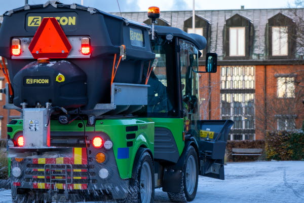 En väg genom en snötäckta allé av träd. Röda flervåningshus i tegel till vänster om vägen. Foto.