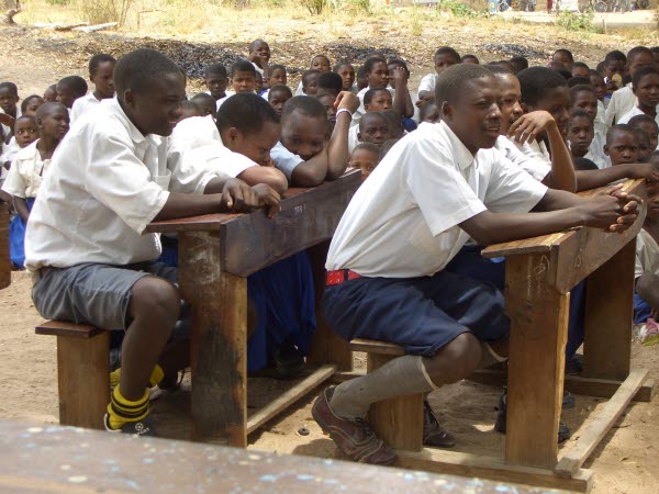 Mörka barn i Tanzania sitter på skolbänkar ute