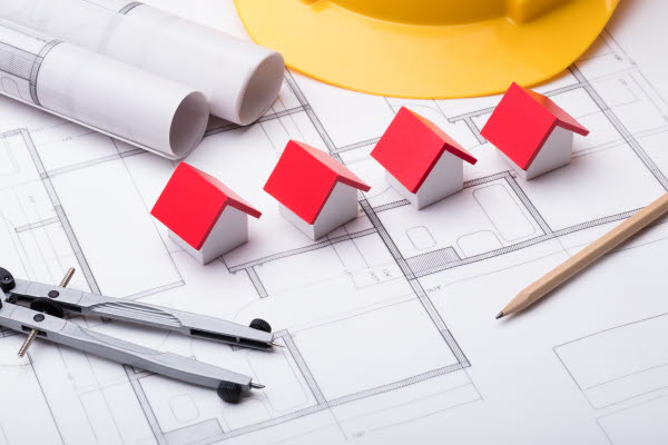 Fyra små låtsashus, penna och rullade ritningar ligger på en utvecklad ritning. Foto.