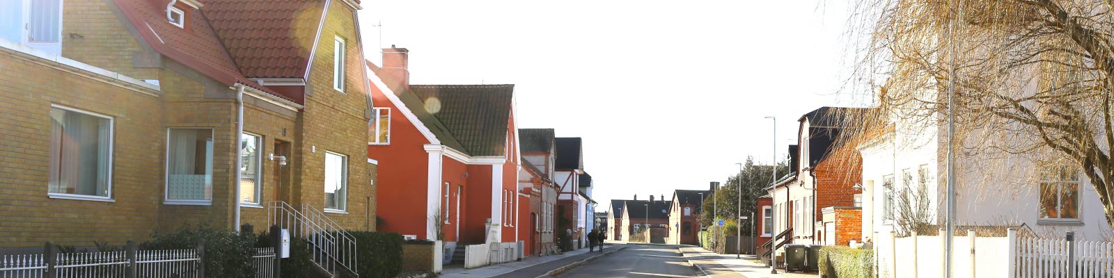Gata med flera färgglada hus i solsken längs sidorna, foto. 
