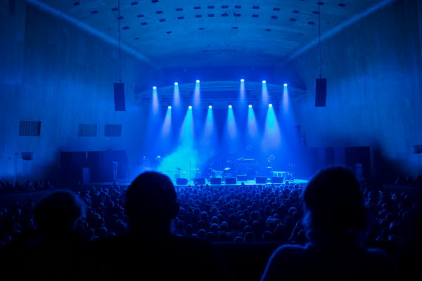 En större publik framför en scen i blått ljus. Foto.