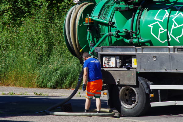 En person håller en lång slang från en lastbil. Foto.