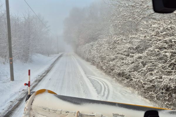 Ett stort fordon med snöskrapa fram framför ett stort tegelhus, kommunhuset. Foto.