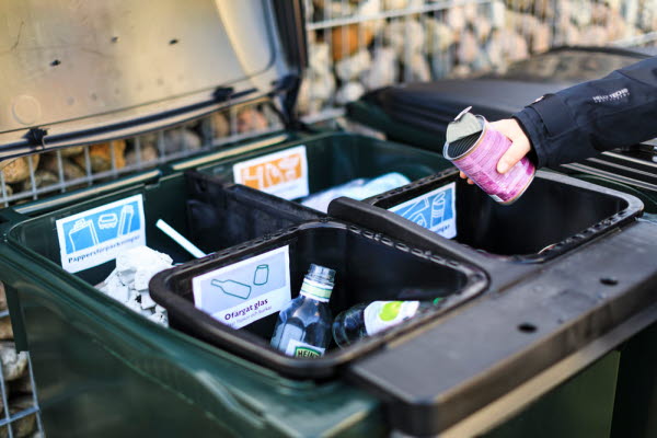 En person slänger en konservburt i en soptunna, som rymmer fyra mindre kärl. Foto.