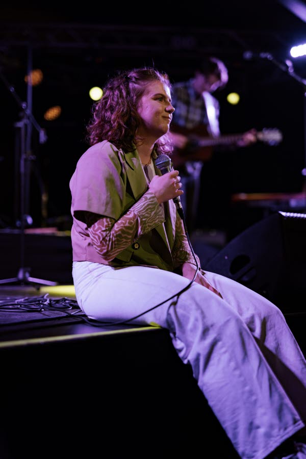 Person sitter på en scen med en mikrofon i handen. Foto.