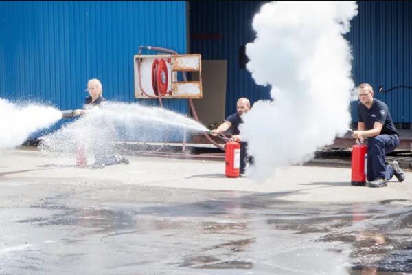 Tre personer sprutar med varsin brandsläckare. Foto.