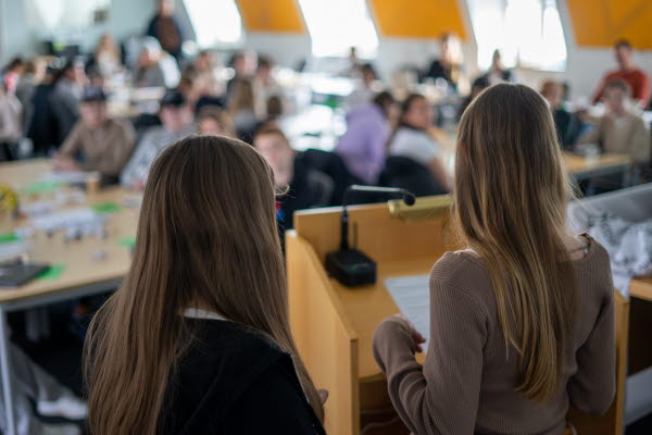 En sal fylld med ungdomar där vissa håller upp gröna lappar. Foto.