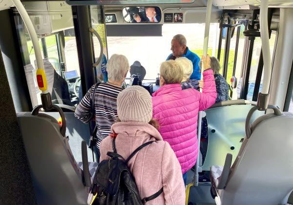 Sex äldre personer står och pratar med chauffören inne i en buss. Foto.  