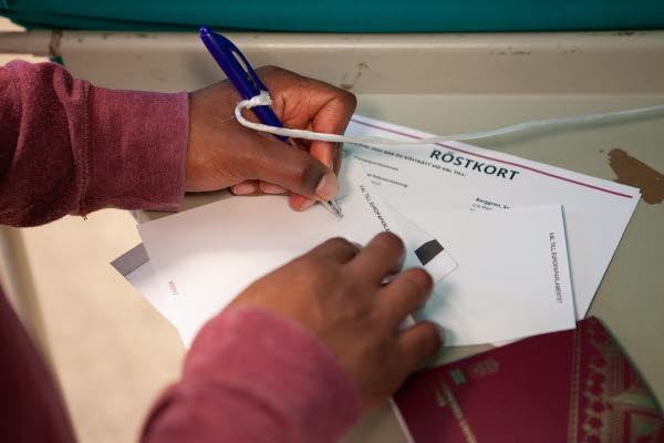 En person skriver på en valsedel i ett röstningsbås. Foto.